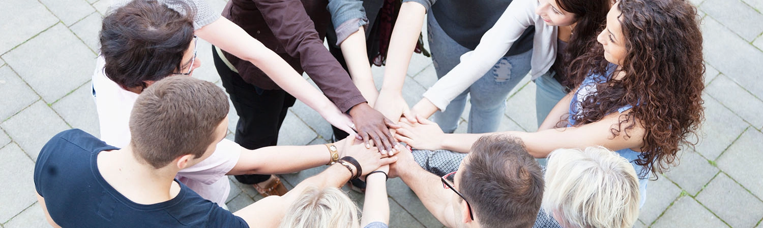 group of people of different ages standing in a circle and touching each other with their hands