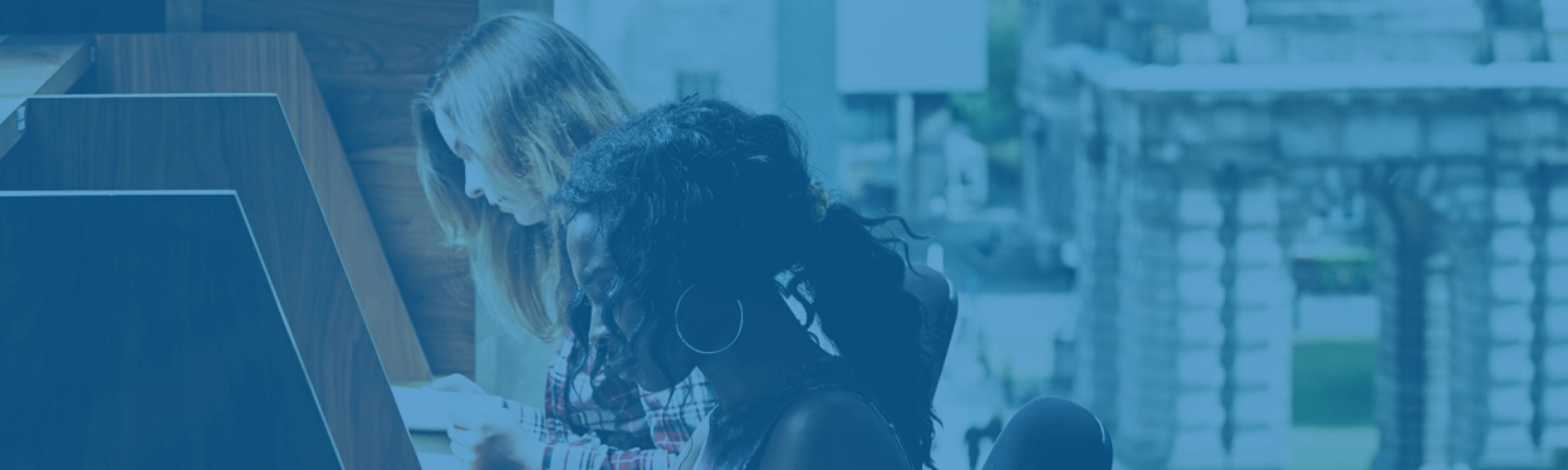 Two students studying at desks. You can see a view of the Bell Tower of Trinity College Dublin through the window