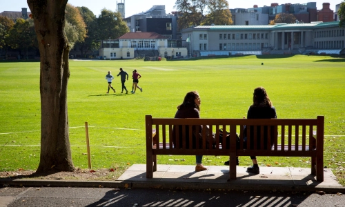 Two Trinity students sitting on grass in conversation.